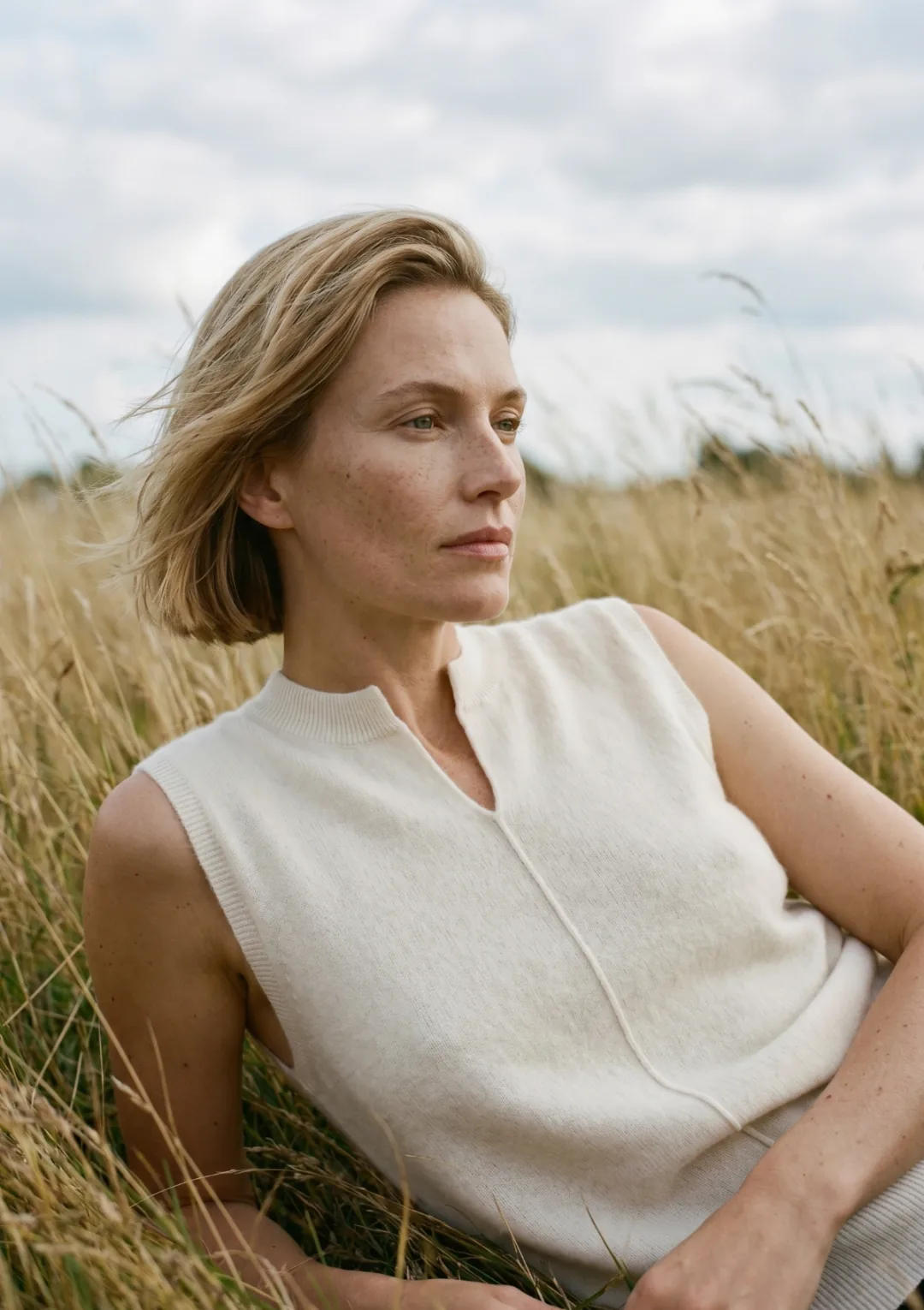 A woman in a cream knitted vest sitting in a field of tall dry grass